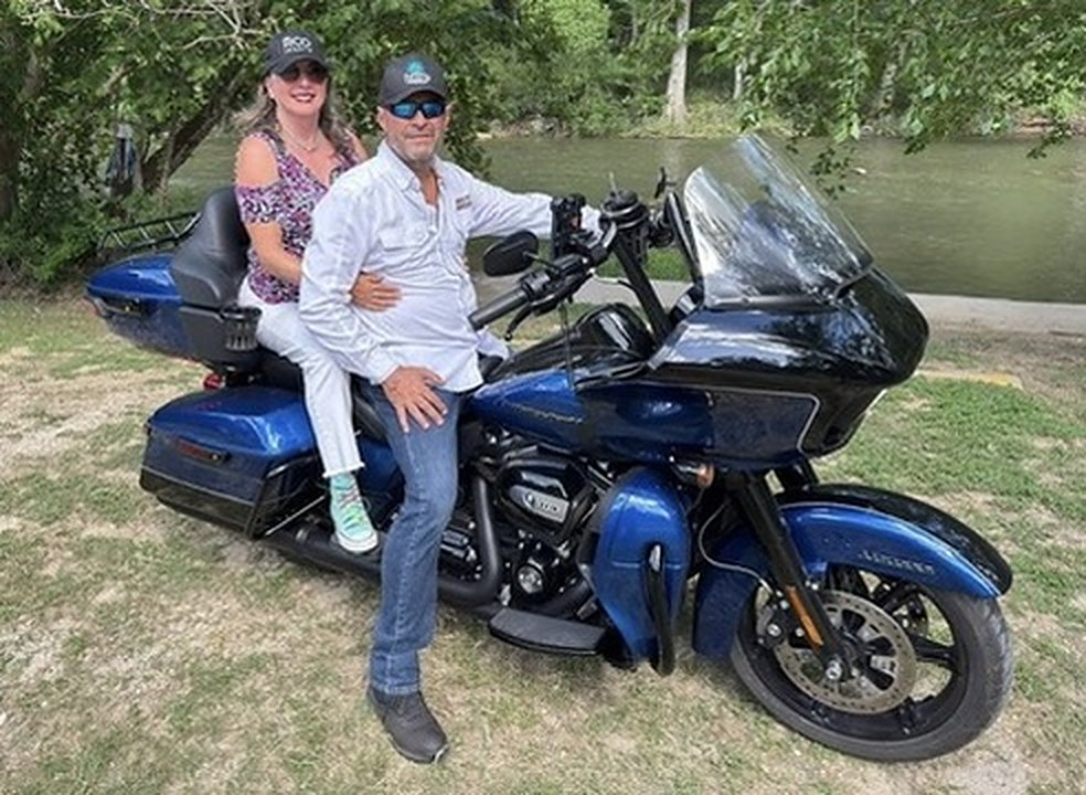 Rick and his wife Sharon on his blue Harley beside a river